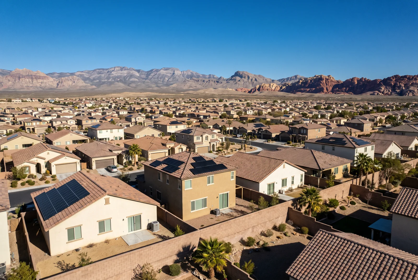 Elevated view of a Las Vegas suburban neighborhood of tile-roofed homes, many carrying rooftop solar arrays, with the mountains behind